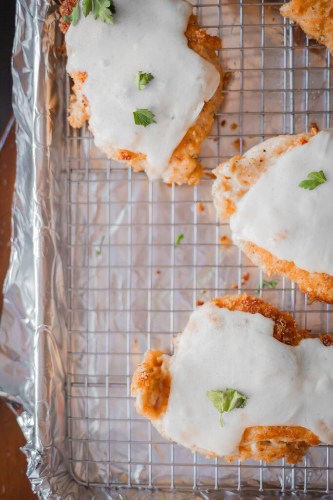 top down view of gluten free breaded chicken with cheese and parsley on top