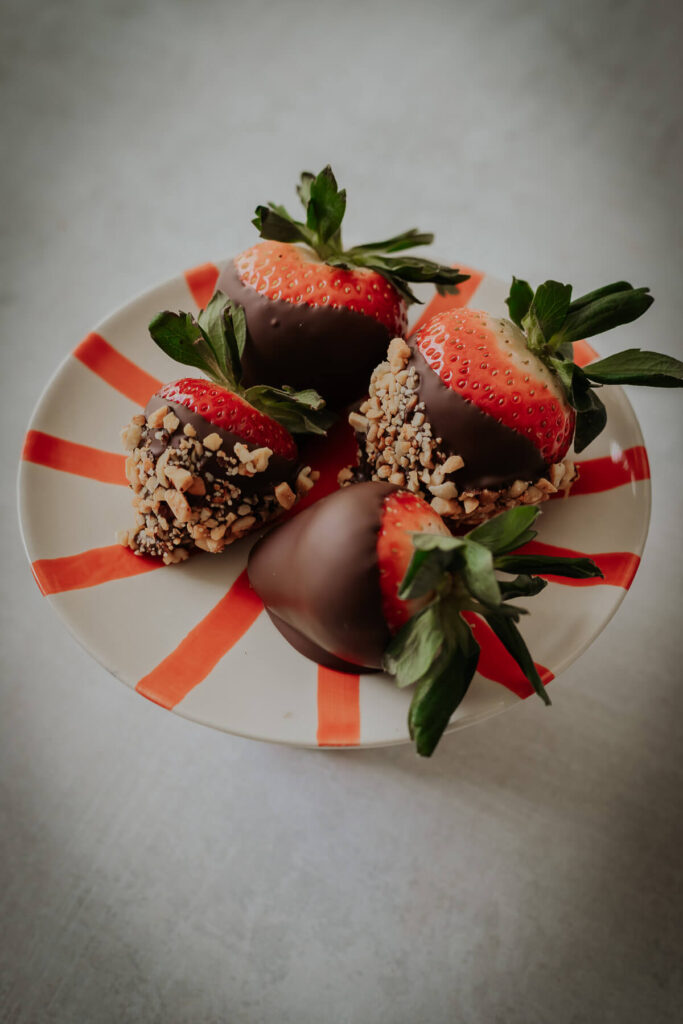 close up view of chocolate covered strawberries with nut toppings - get the recipe inside!