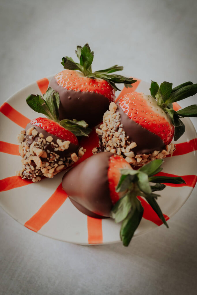 close up view of chocolate covered strawberries with nut toppings - get the recipe inside!